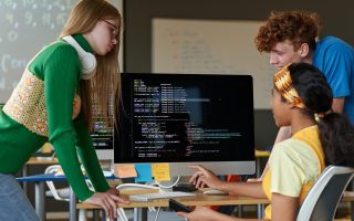 Group of students sitting in front of monitor and working over computer codes in team during IT lesson